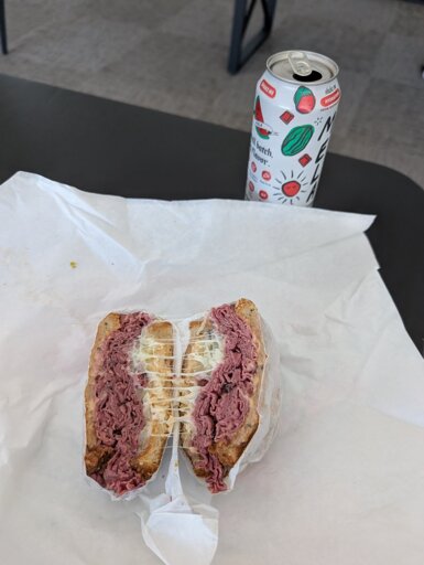A pastrami sandwich sliced in half, with gooey strands of swiss cheese connecting the two sides.