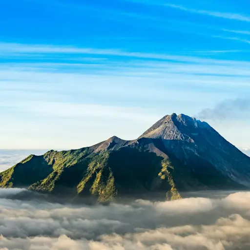 Photo of a volcano with clouds at the base of the mountain, with slight smoke from the peak.